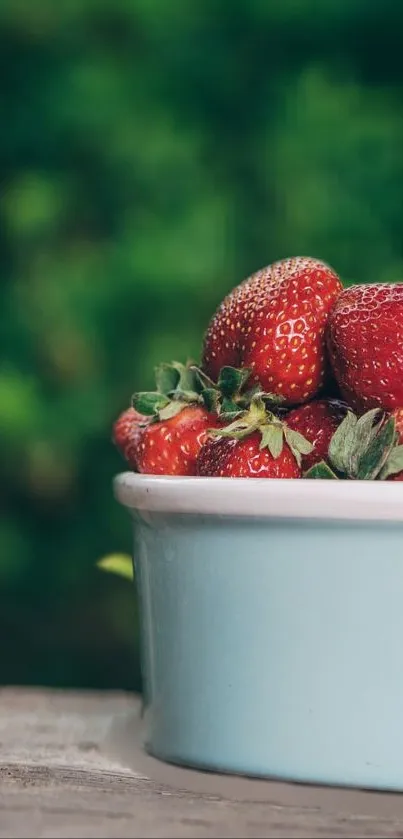 Bowl of red strawberries on a table with green background.