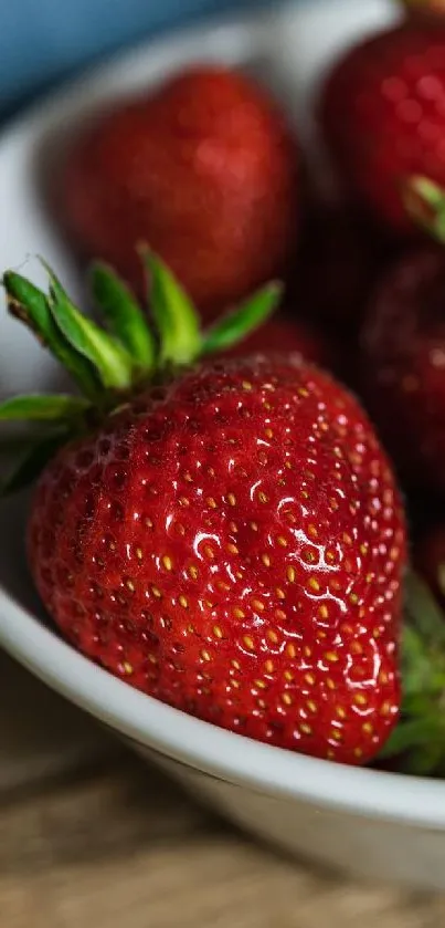 A white bowl filled with fresh red strawberries on a wooden surface.