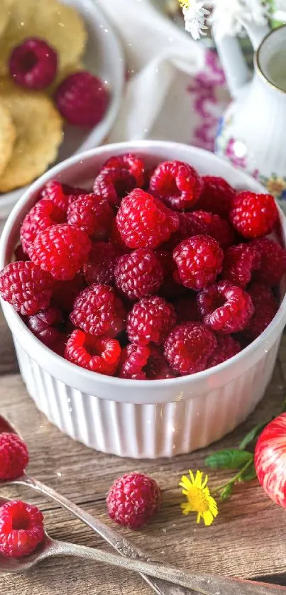 Vibrant red raspberries in a bowl with apples and flowers on a rustic table.