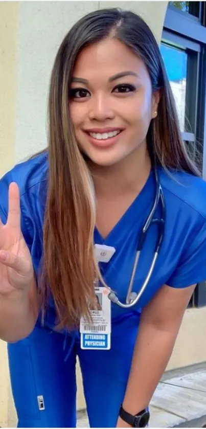 Smiling nurse in blue scrubs with a peace sign pose.