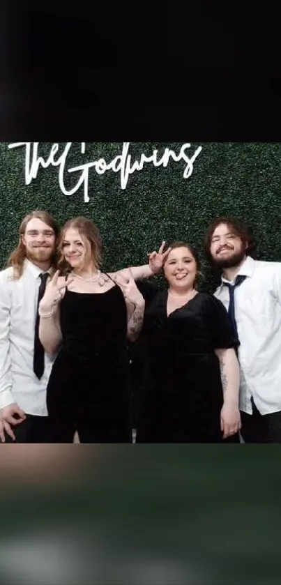 Four friends pose happily in front of a green backdrop at an event.