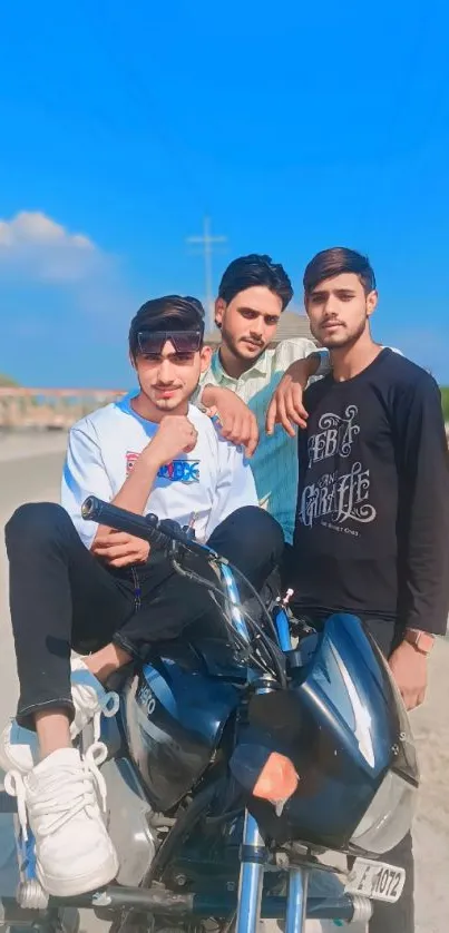 Three friends sitting on a motorcycle under a bright blue sky.