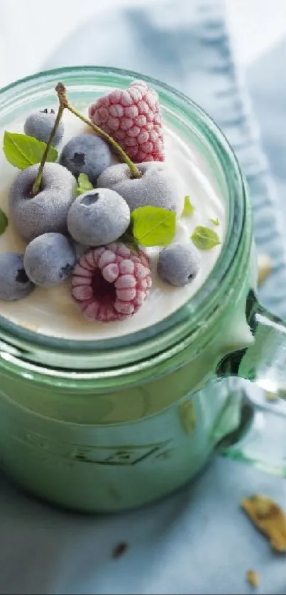 Frozen berries and leaves atop smoothie in green jar with light blue cloth.