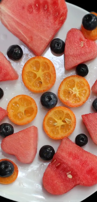 Heart-shaped watermelon with citrus and blueberries on a white plate.