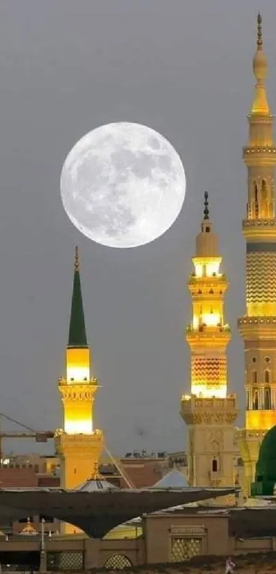 Full moon over mosque towers with a gray night sky backdrop.