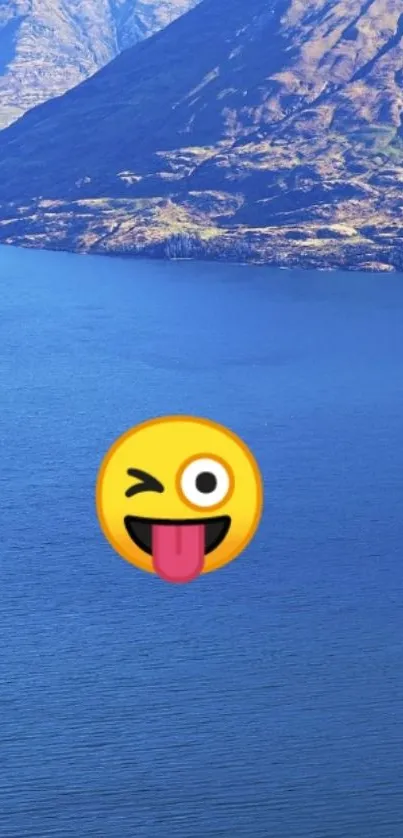 Mobile wallpaper with winking emoji over a blue lake and mountain background.