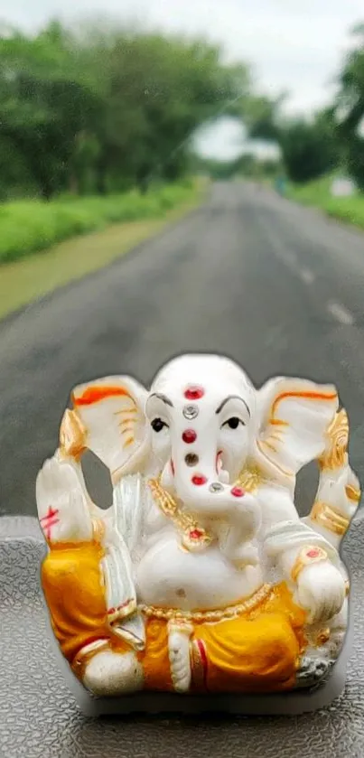 Ganesha idol on car dashboard with road view.