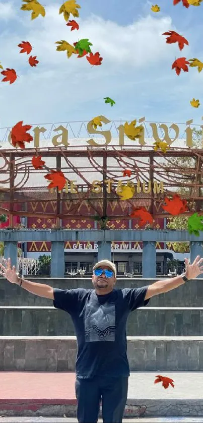 Man joyfully posing at Gelora Sriwijaya Stadium entrance under blue sky.