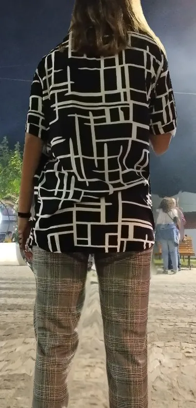 Back view of person wearing geometric patterned shirt in night street setting.