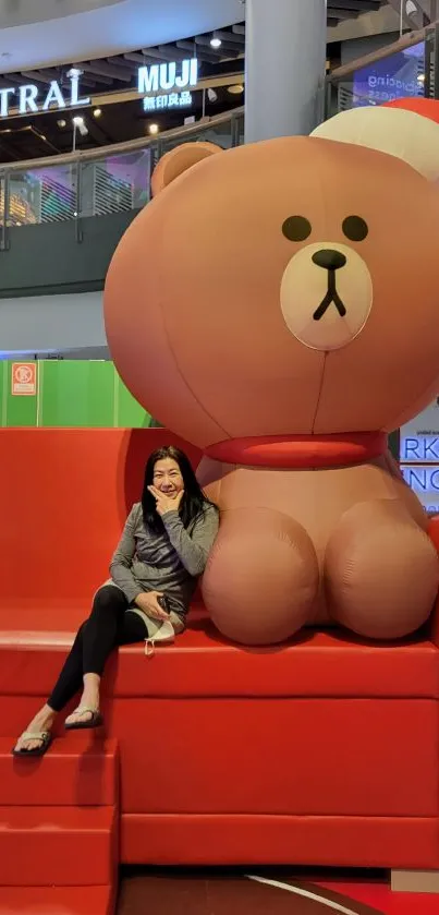 Giant teddy bear sitting on a vibrant red sofa in a mall setting.