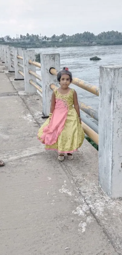 Young girl in a colorful dress standing on a river bridge, scenic background.