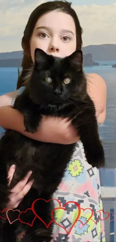 Girl holding a black cat with a scenic ocean backdrop.