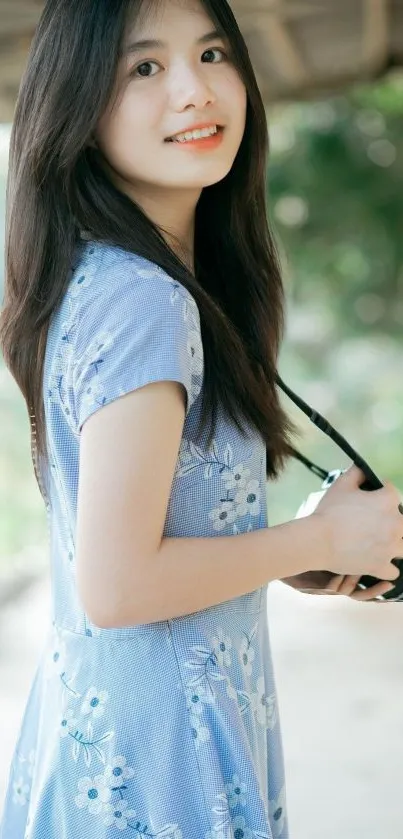 Young woman in blue dress holding a camera outdoors.