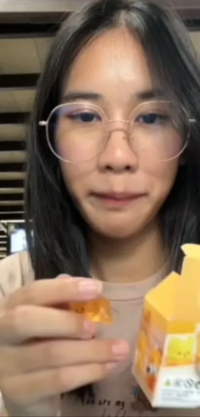 Woman with glasses holding a small box indoors.