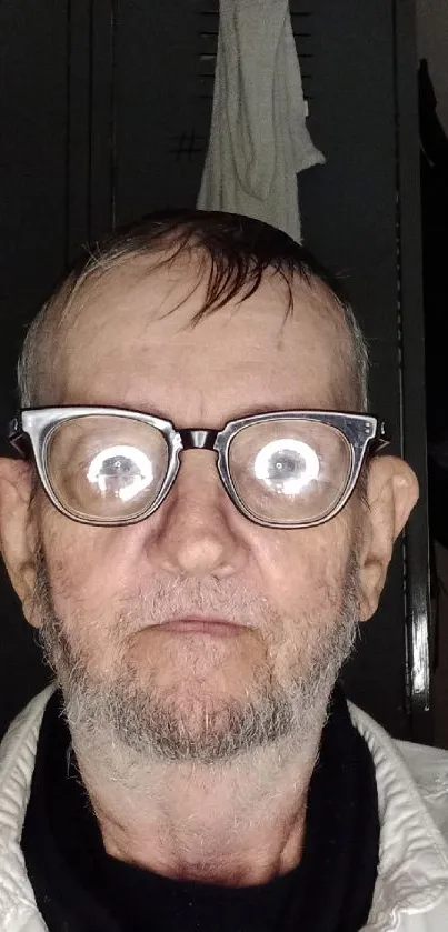 Portrait with glasses reflecting light on a muted gray background.