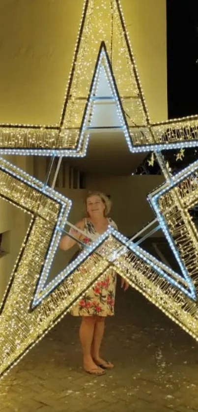 Woman standing inside a glowing star light display at night.