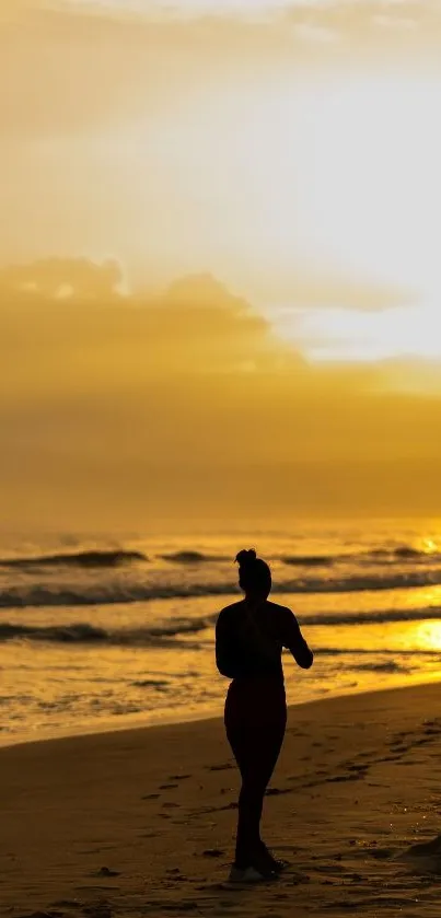 A silhouette on a beach during a golden sunset over calm ocean waves.