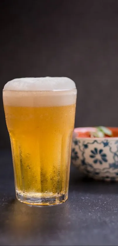 Golden beer glass with frothy top on dark surface.