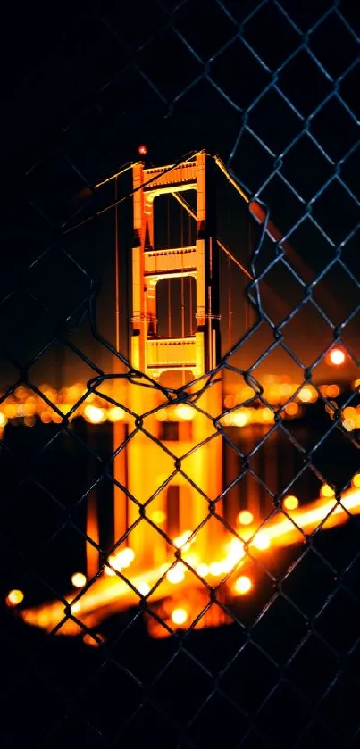 Golden Gate Bridge glowing at night through a chain-link fence.