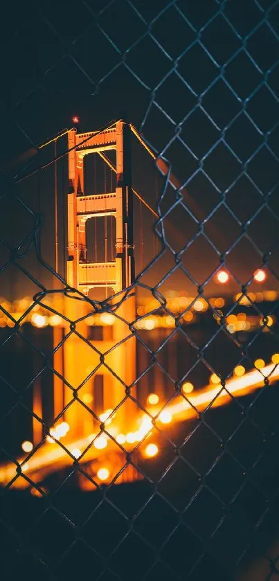 Golden Gate Bridge at night through a chain-link fence, glowing against the dark sky.