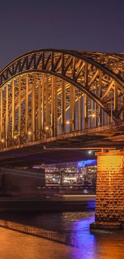 Golden-lit bridge at night with reflection on river.