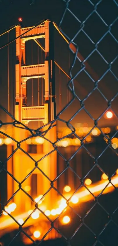 Golden Gate Bridge at night through a fence, glowing with city lights.