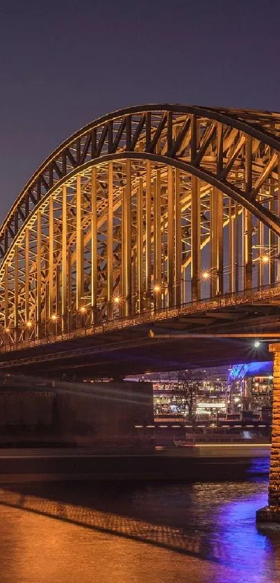 A golden-lit bridge at night over water, reflecting city lights.