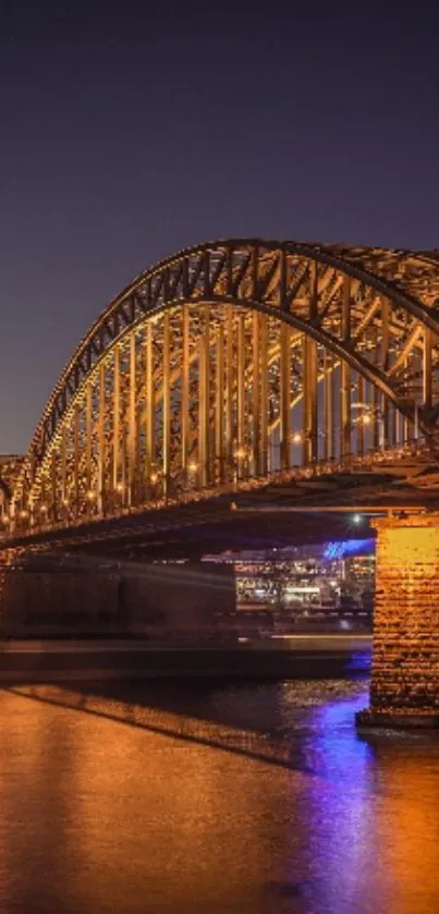 Golden bridge at night with reflections on the water under a clear sky.