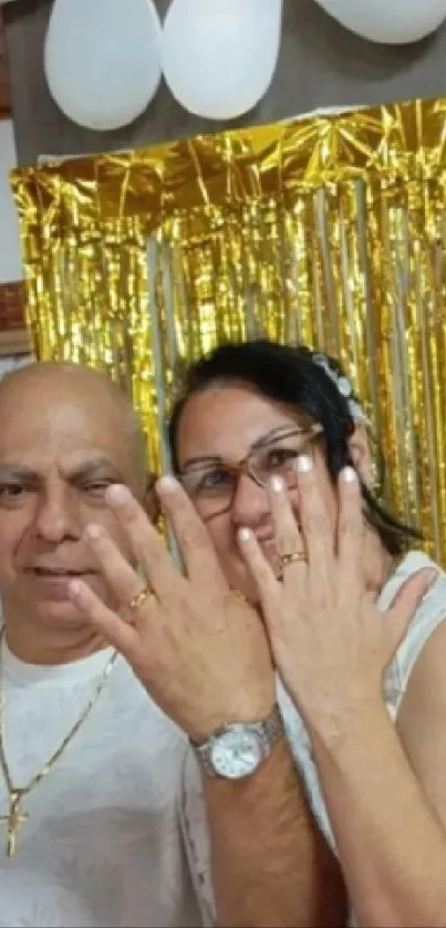 Two people celebrating with gold backdrop and rings displayed.