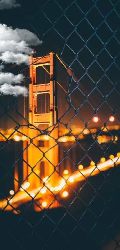 Golden Gate Bridge illuminated at night through a fence, city lights glowing.