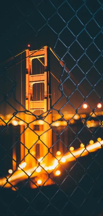 Golden Gate Bridge illuminated at night behind a chain-link fence.