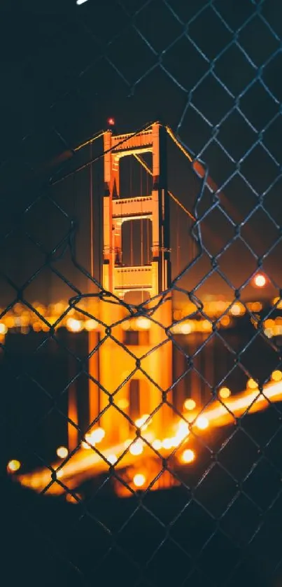 Night view of Golden Gate Bridge behind a chain link fence with glowing lights.