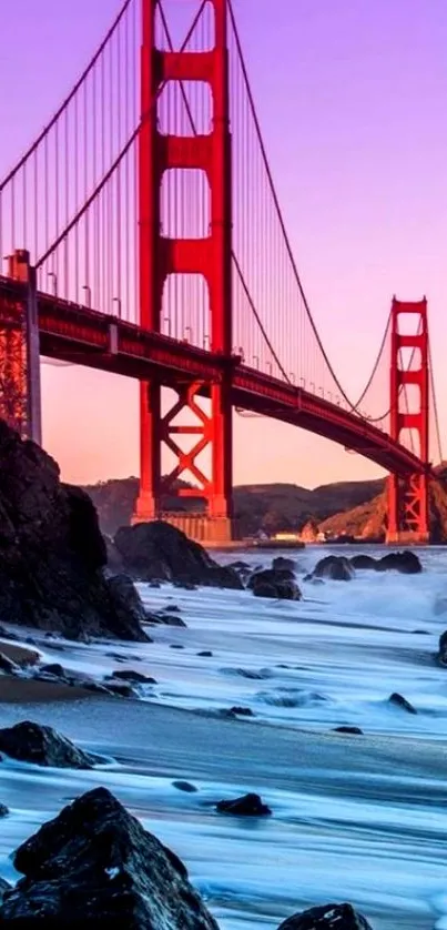 Golden Gate Bridge at sunset with purple sky and rocky shore.