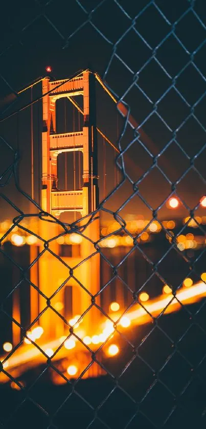 Golden Gate Bridge at night through a fence, glowing with lights against a dark sky.