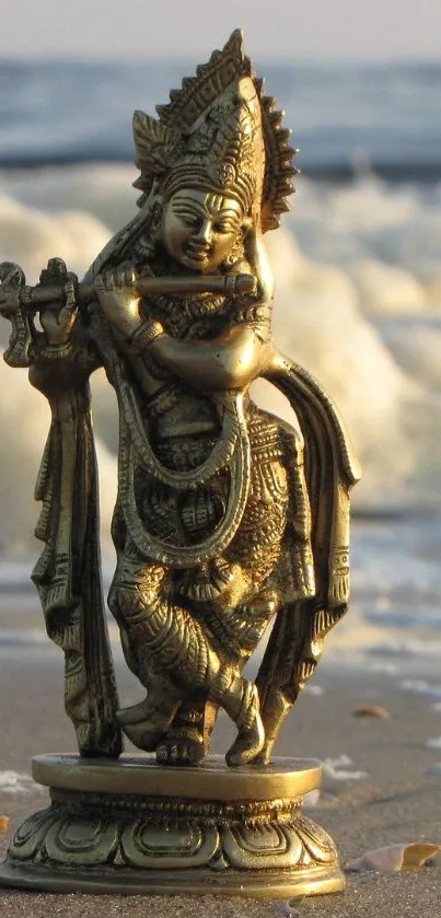 Golden Krishna statue on a beach with ocean waves in the background.