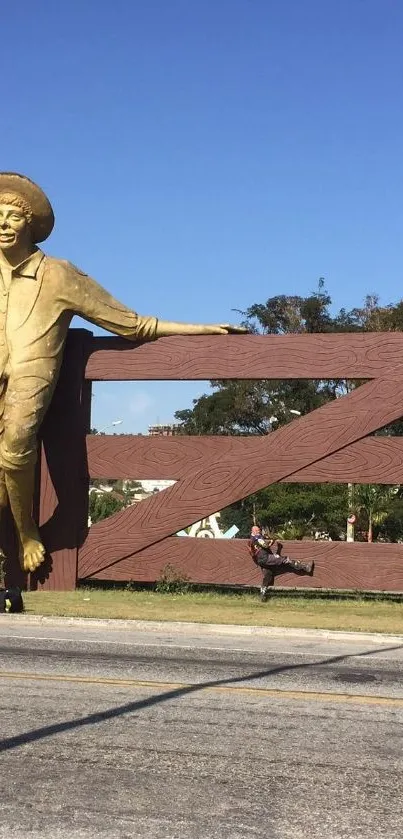 Golden statue leaning on brown gate under a clear blue sky.