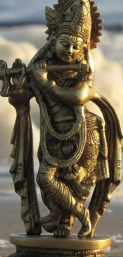 Golden statue of Lord Krishna playing the flute on a beach.