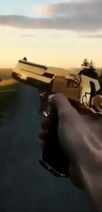 Hand holding a golden gun against a scenic sunset backdrop.