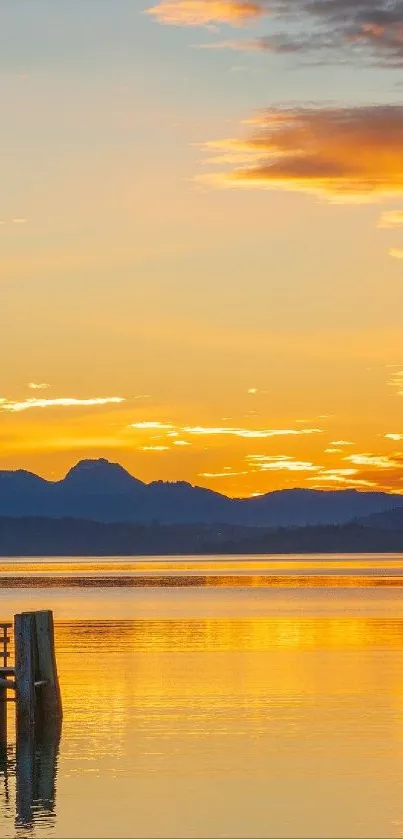 Golden sunset over a calm lake with mountains in the background.