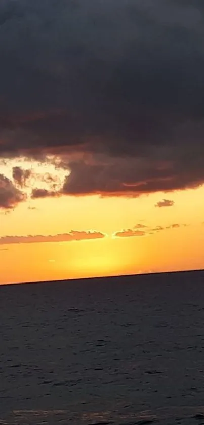 Golden sunset over calm ocean with dramatic clouds.