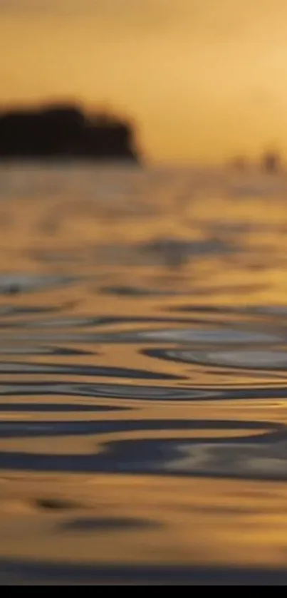 Golden sunset reflecting over serene ocean waves with silhouette in the distance.