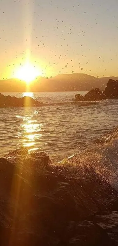 Golden sunset over ocean waves with rocky shoreline.