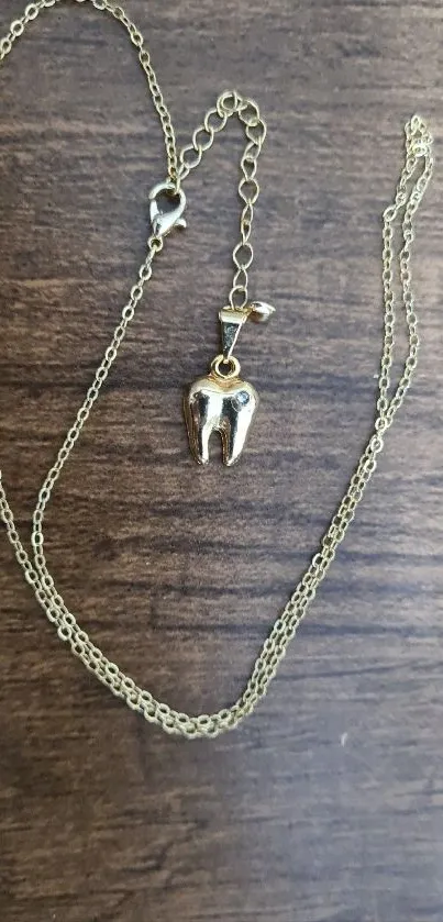 Gold tooth pendant necklace on wood background.