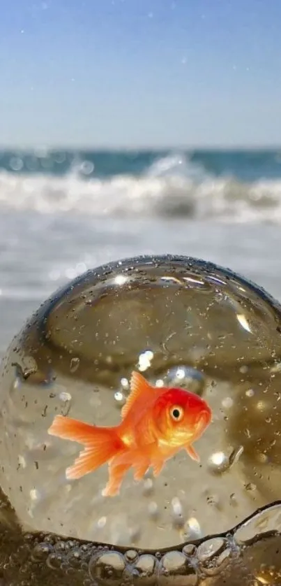 Goldfish in a glass sphere on a sunlit beach with ocean waves.