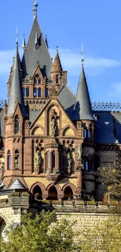 Gothic castle with spires against a blue sky, surrounded by greenery.