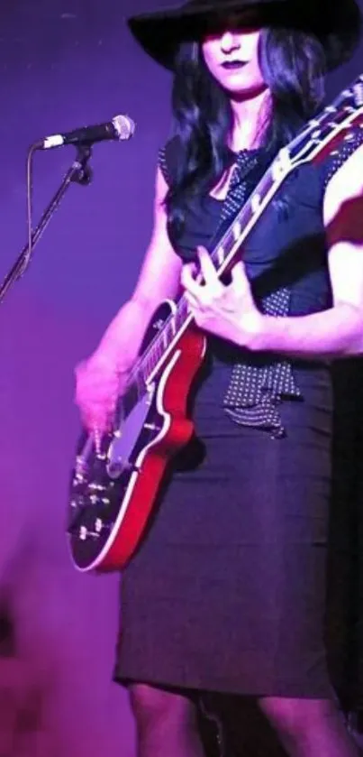 Gothic guitarist in a dress playing electric guitar on stage with purple background.