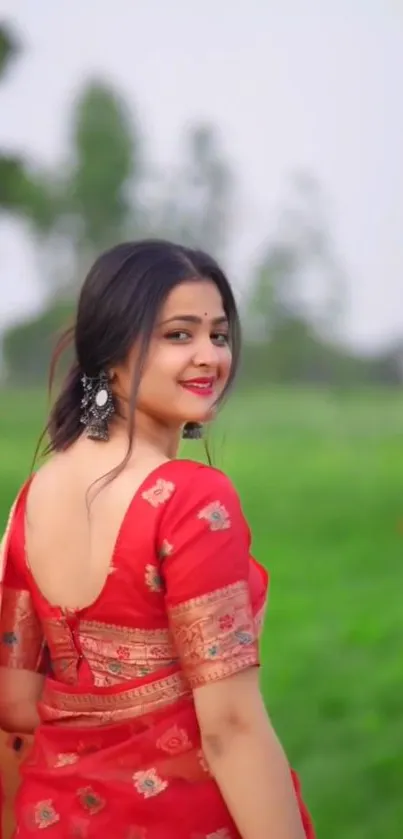 Woman in a red saree against a green field backdrop.