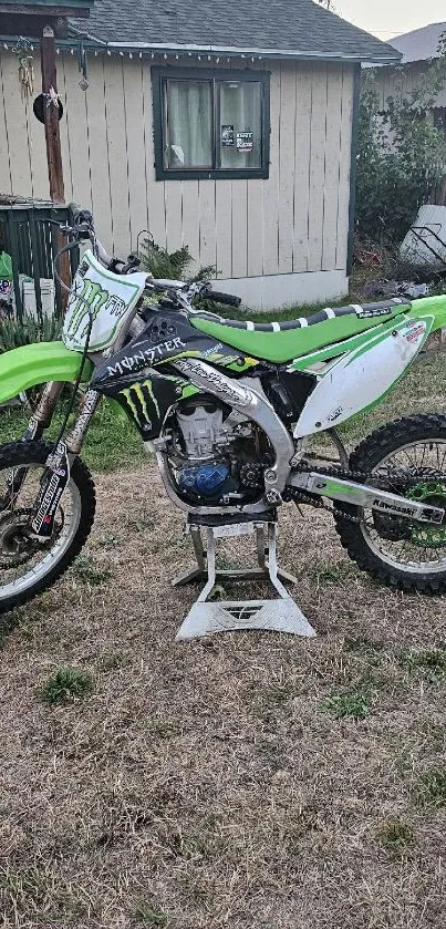 Green dirt bike in a rustic backyard setting on a stand.