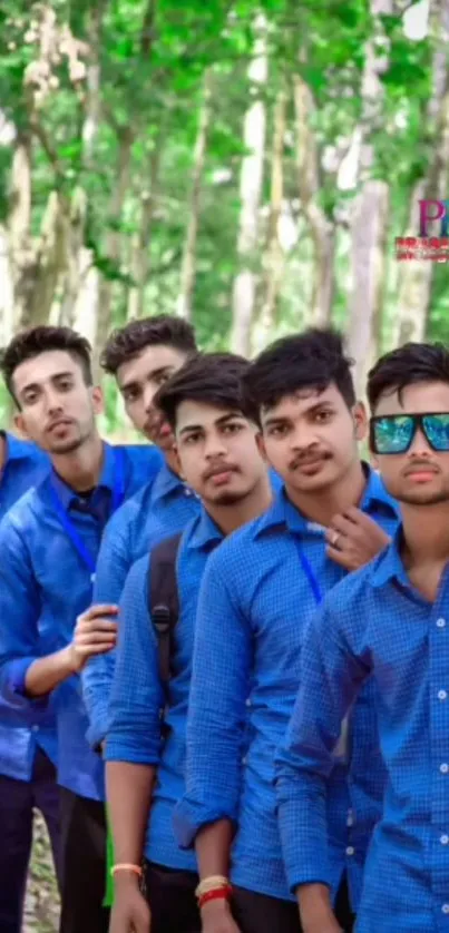 Group of friends in blue shirts posing in a lush, green forest setting.