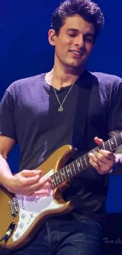 Guitarist playing on stage with a blue background.